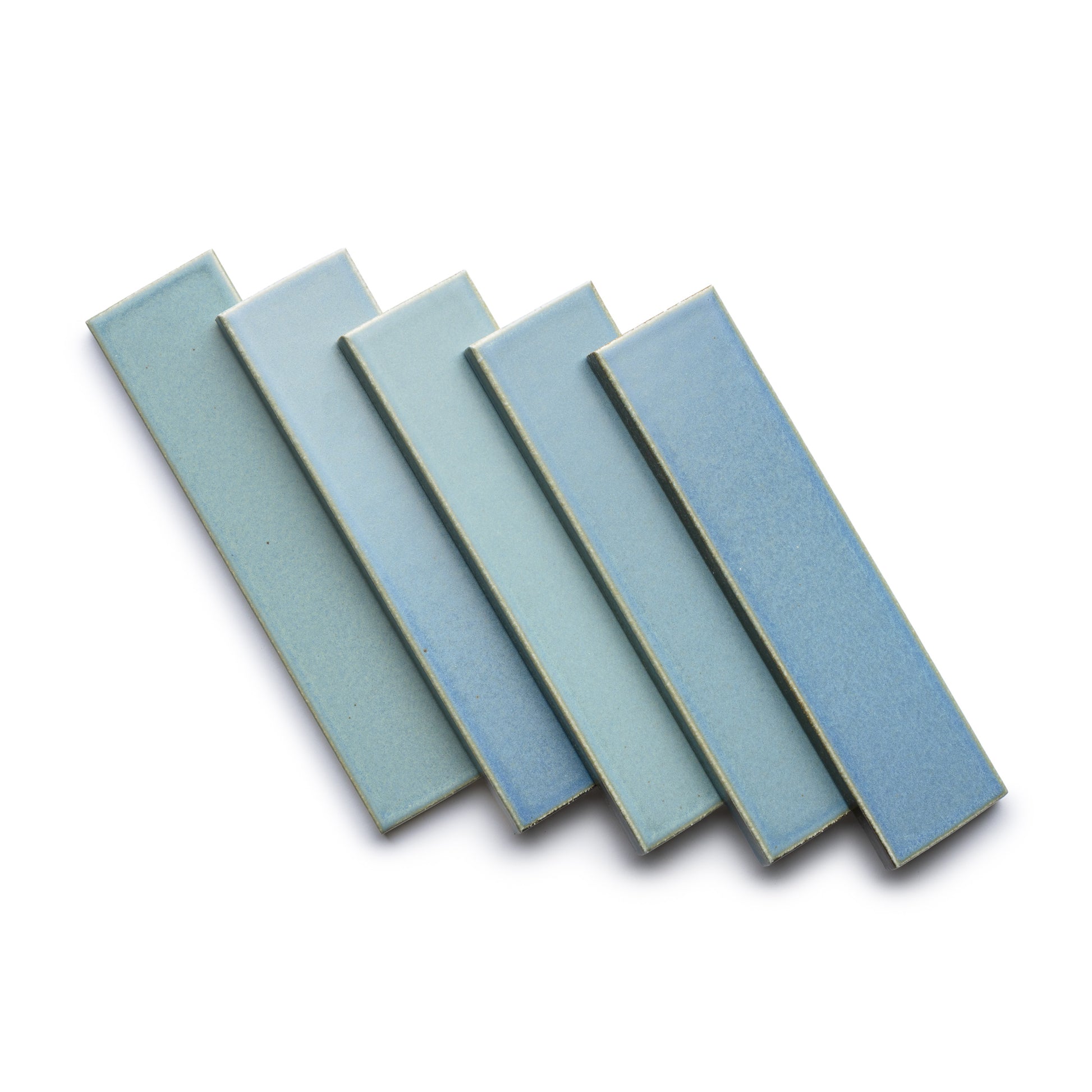 Five rectangular Morning Light + Flat ceramic tiles by Zia Tile are arranged in a fan shape on a white background, each featuring subtle texture and varying light blue shades.