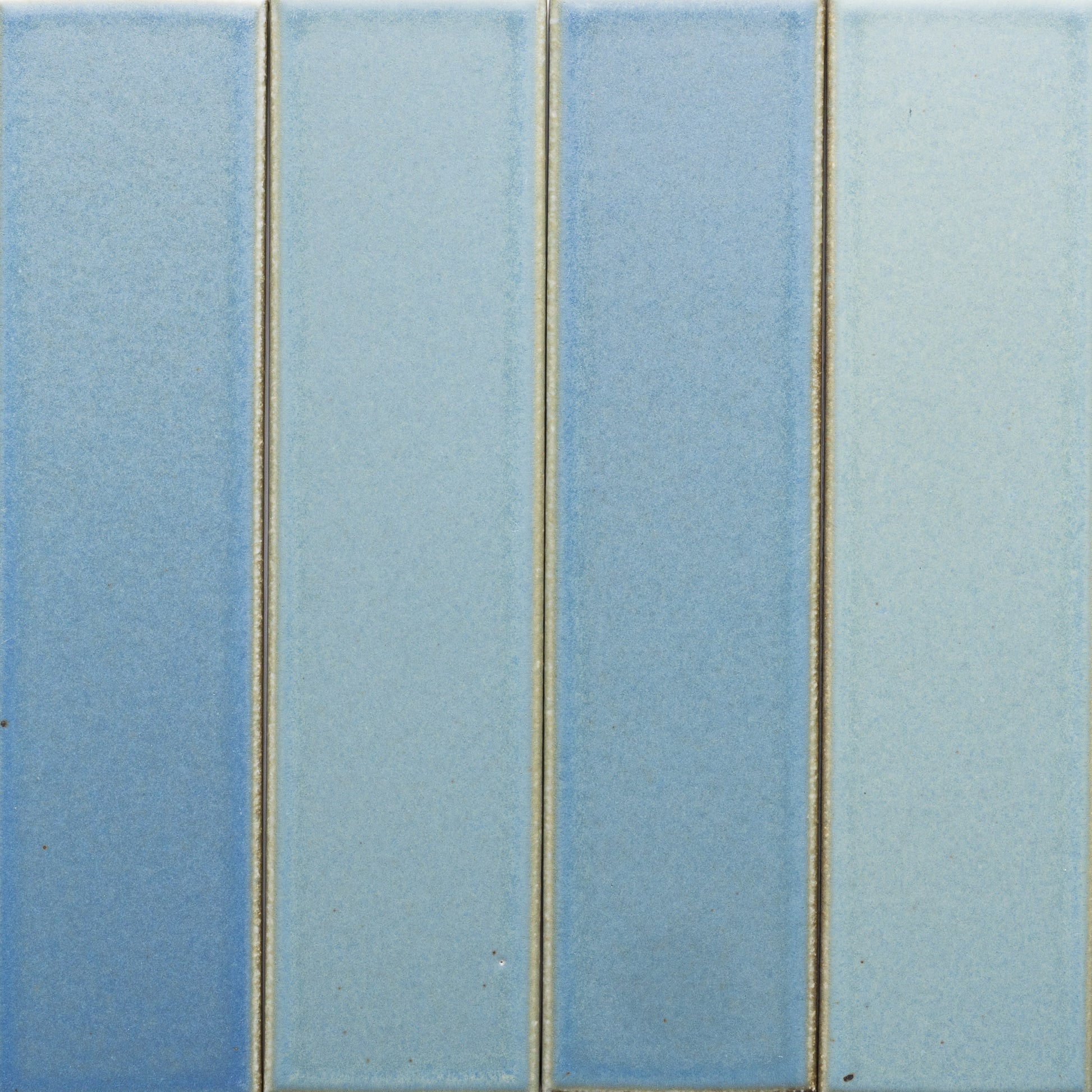 Four vertical rectangular Morning Light + Flat tiles by Zia Tile, in varying blue shades, are arranged side by side with thin, slightly raised grout lines. The tiles have a smooth, matte surface.