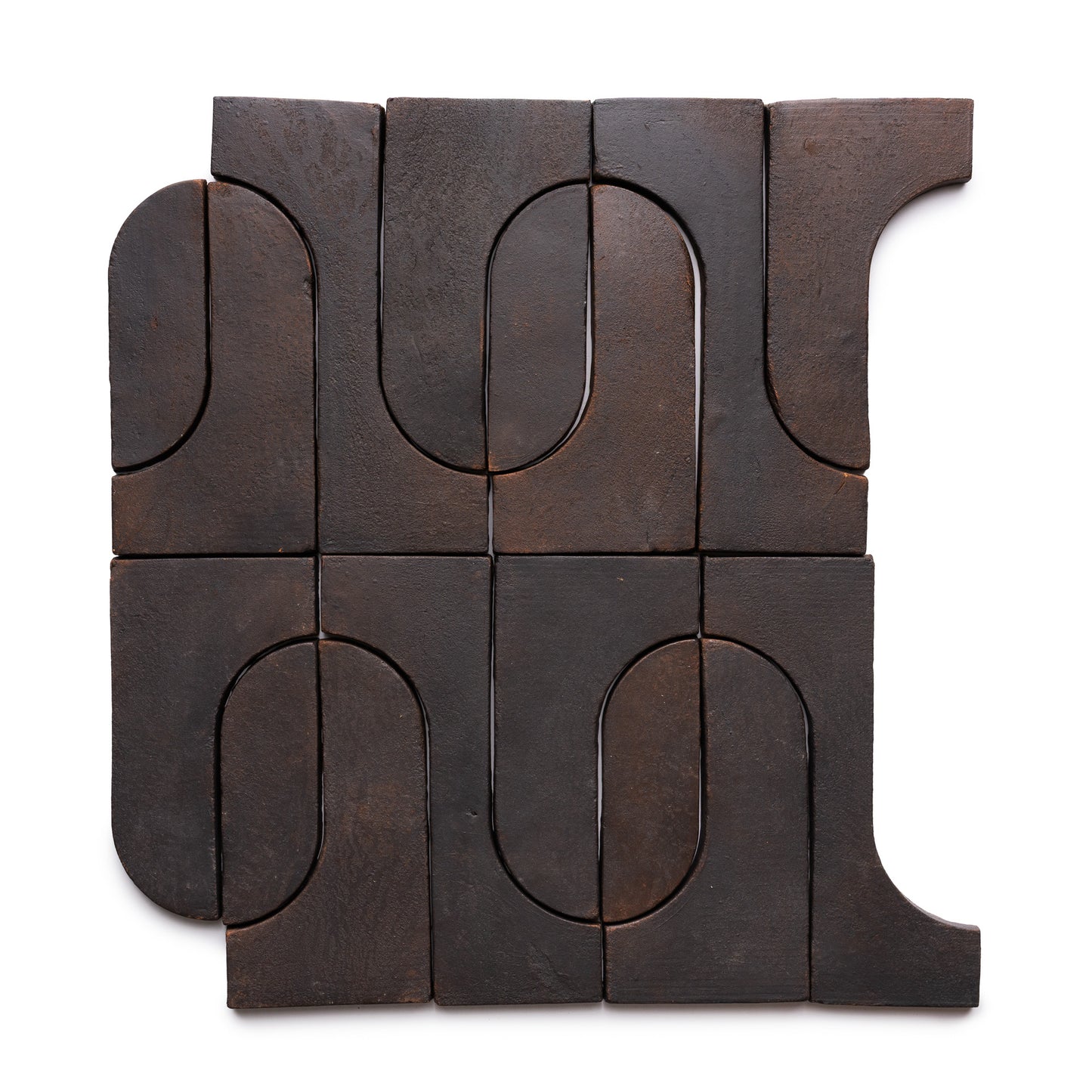 Twelve Durango + Oscura tiles from Zia Tile form a square, featuring dark brown ceramic with curved and straight indents that create an abstract, interlocking geometric pattern on a white background.