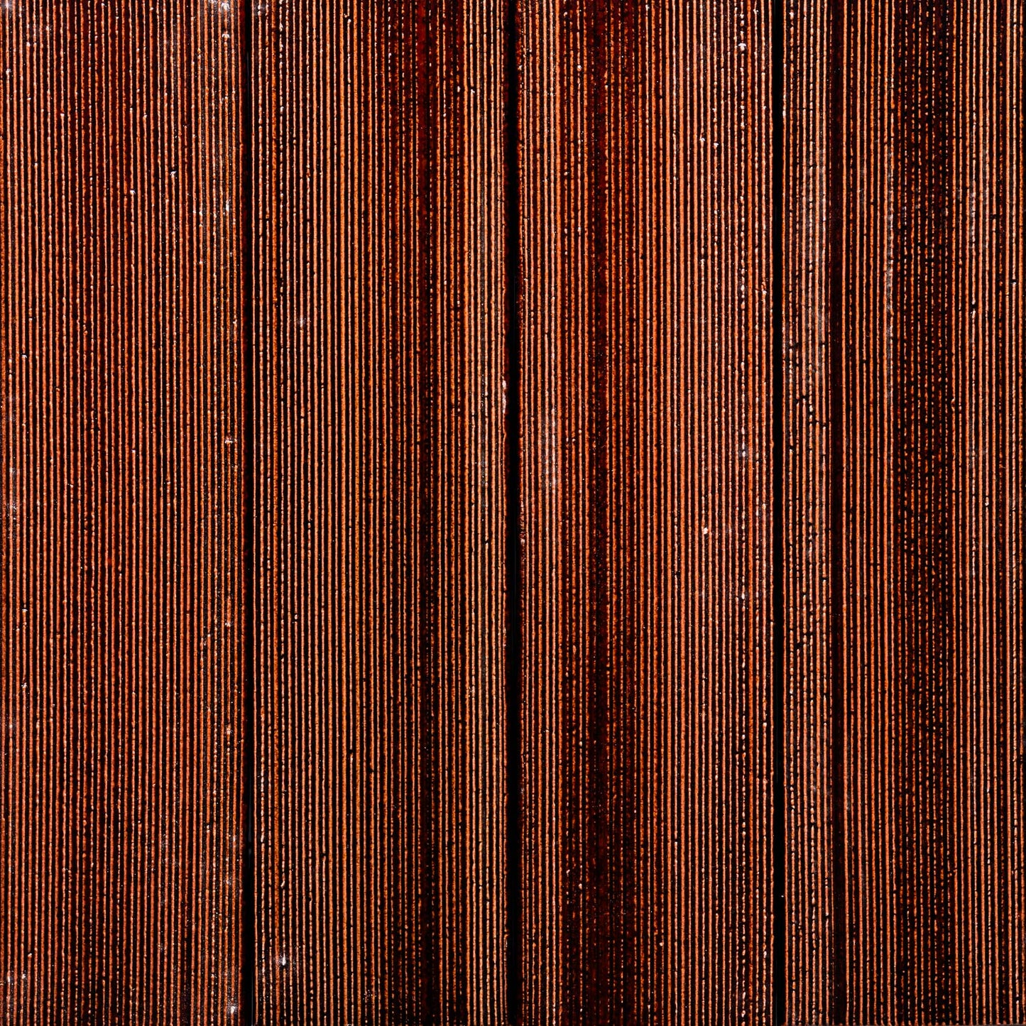 Close-up of Zia Tile's Oxblood + Etched: vertically aligned, tightly packed reddish-brown tiles with fine grooves, forming a distinctive striped pattern.
