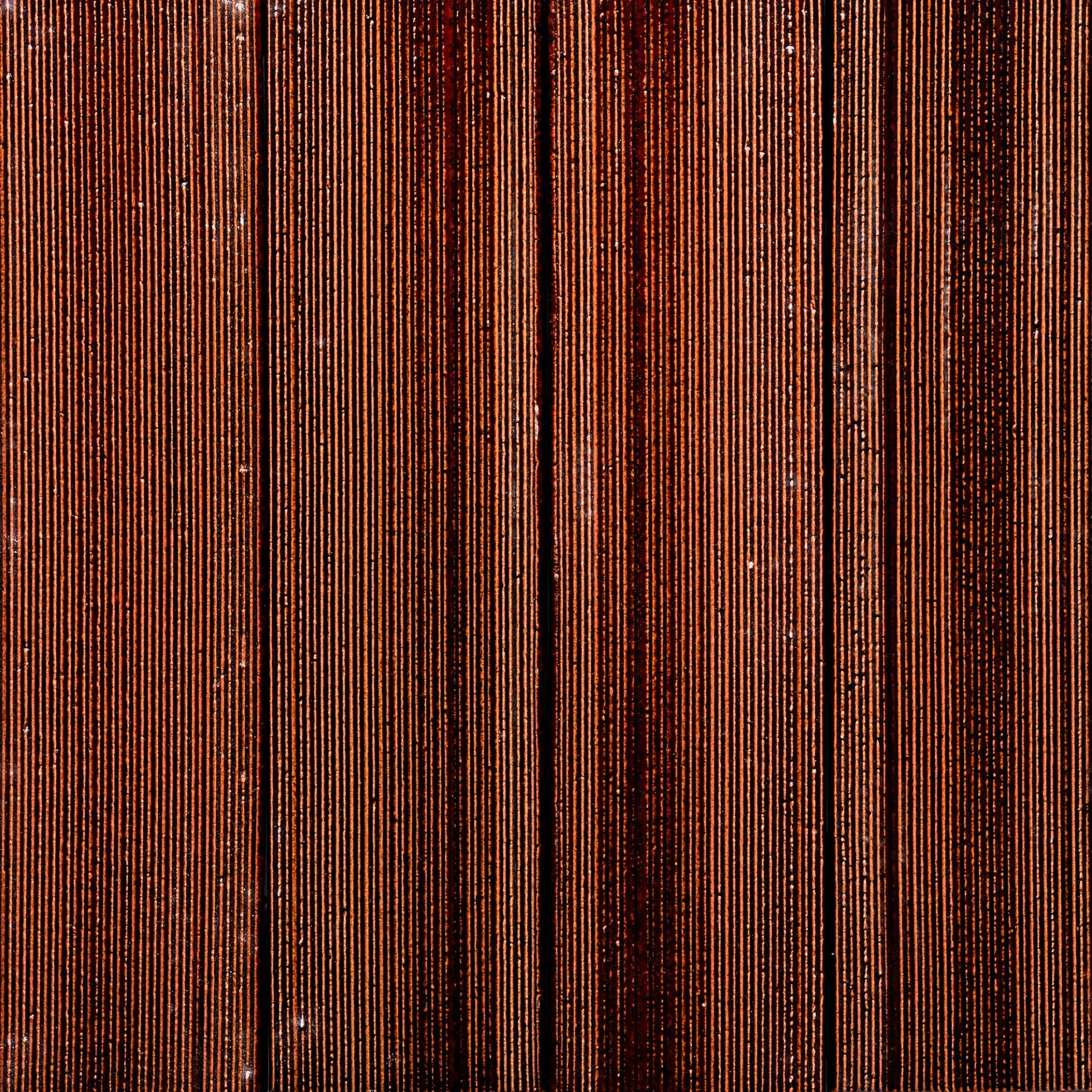 Close-up of Zia Tile's Oxblood + Etched: vertically aligned, tightly packed reddish-brown tiles with fine grooves, forming a distinctive striped pattern.