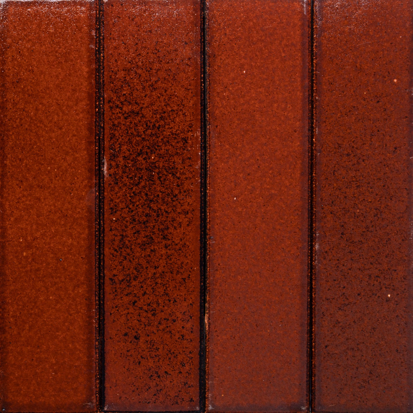 A close-up of four vertical, rectangular Oxblood + Flat ceramic tiles by Zia Tile, featuring a glossy, reddish-brown finish with slight speckling and thin grout lines.