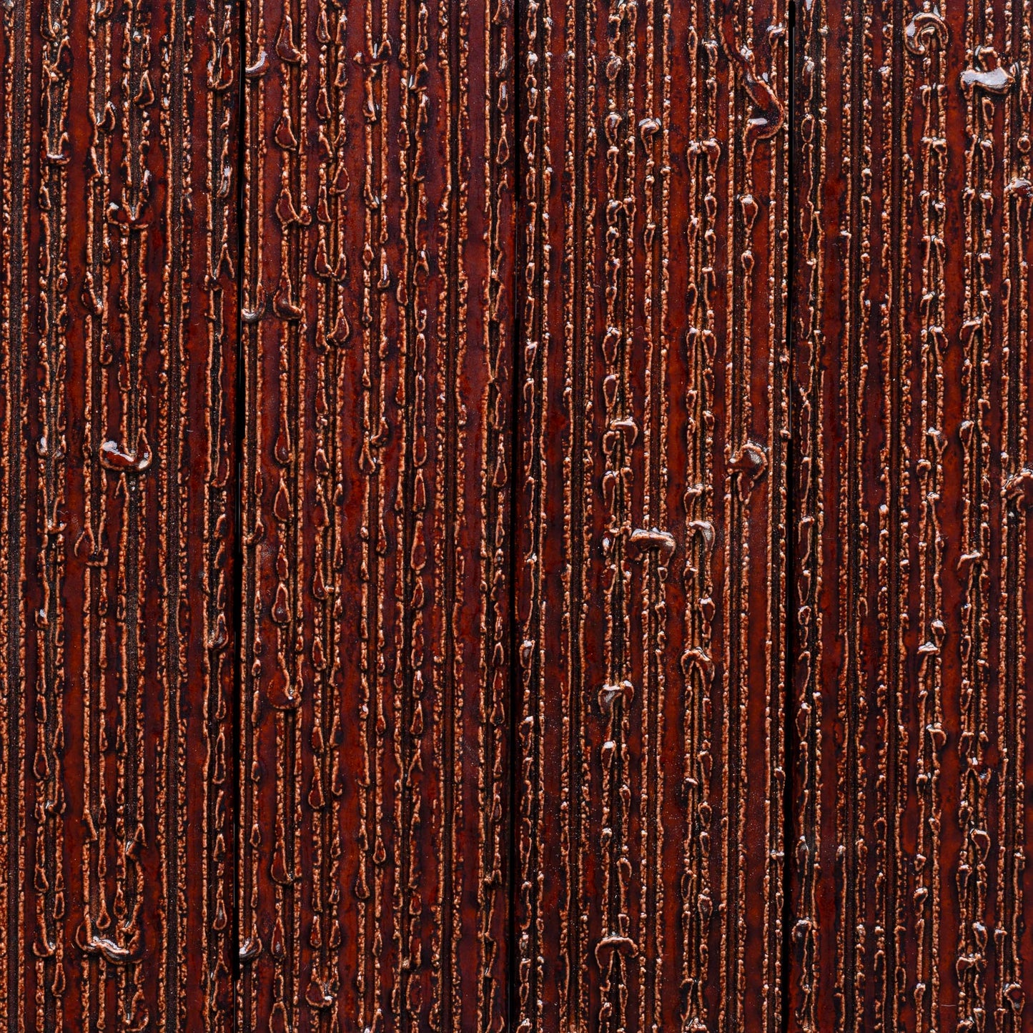 Close-up of Zia Tile’s Oxblood + Furrowed tile, featuring a textured brown surface with vertical shiny, raised ridges and lines for an abstract, tactile pattern.