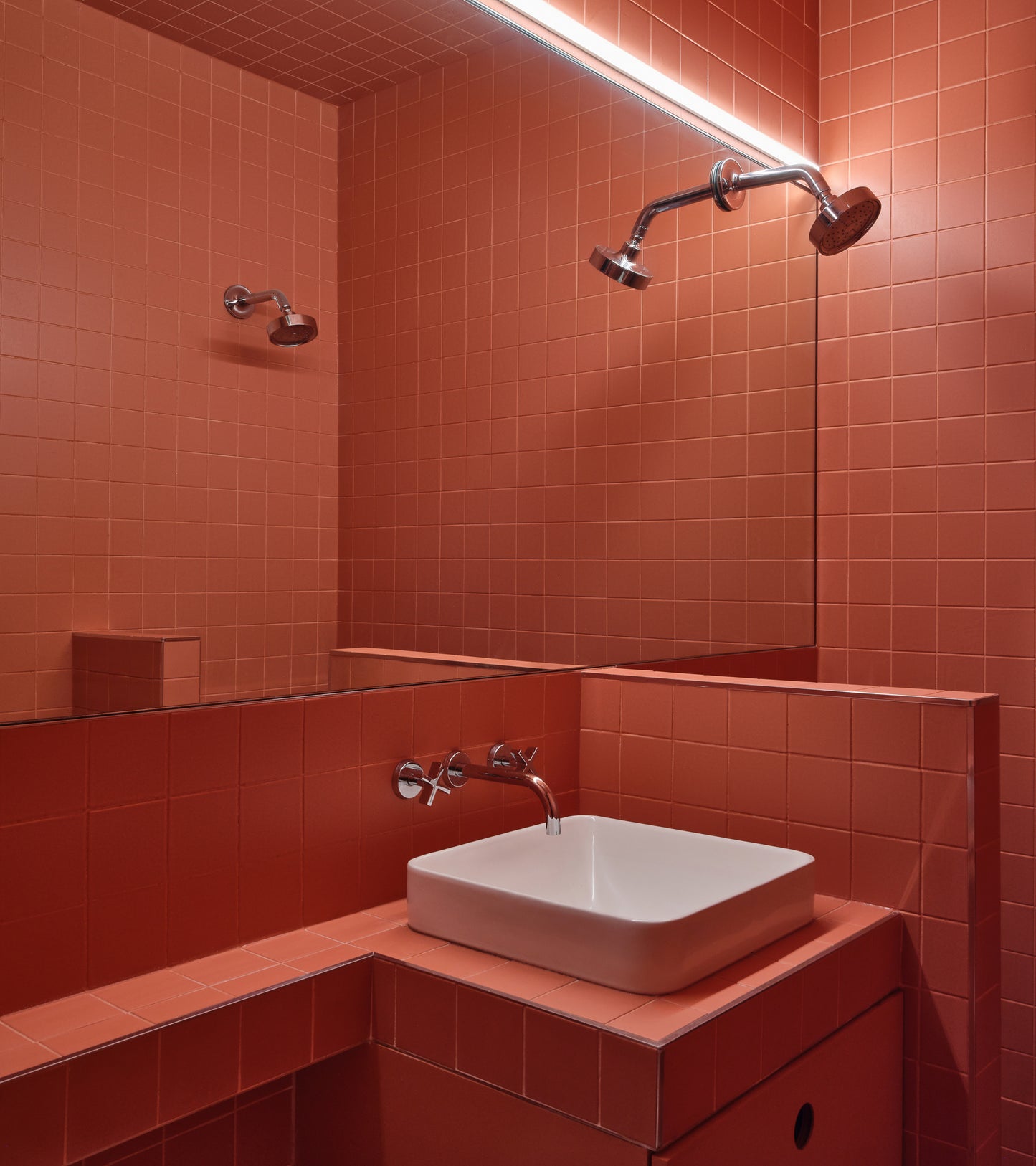 A bathroom fully tiled with Zia Tile's Pink Dahlia 4x4, featuring a wall-mounted sink with a white basin, modern faucet, dual showerheads, a large mirror, and bright lighting to amplify the bold, monochrome look.