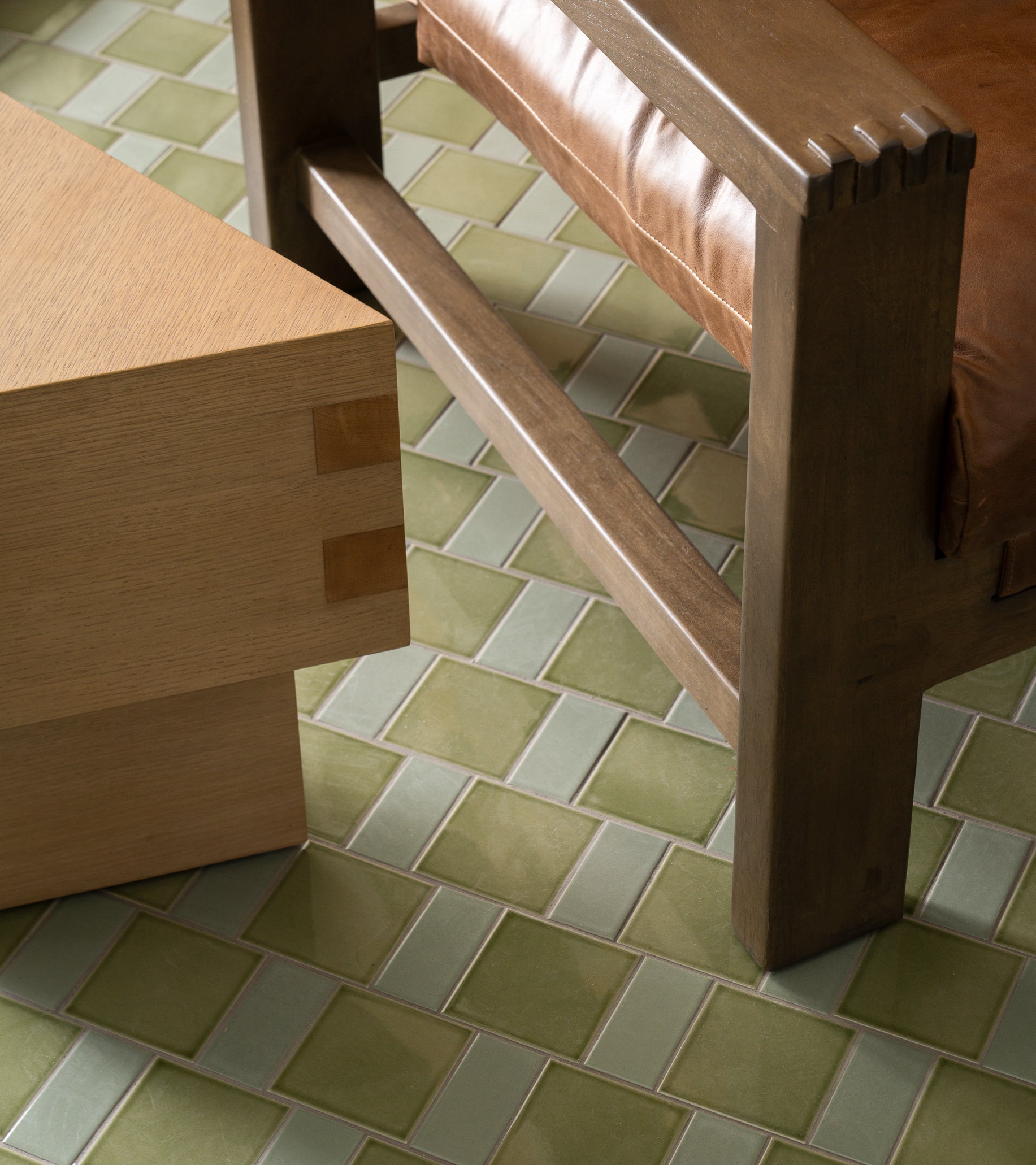 Close-up of a wooden chair with a brown leather cushion and a light wooden table on Zia Tile’s Ponderosa 4x4 green architectural grade ceramic tiles.