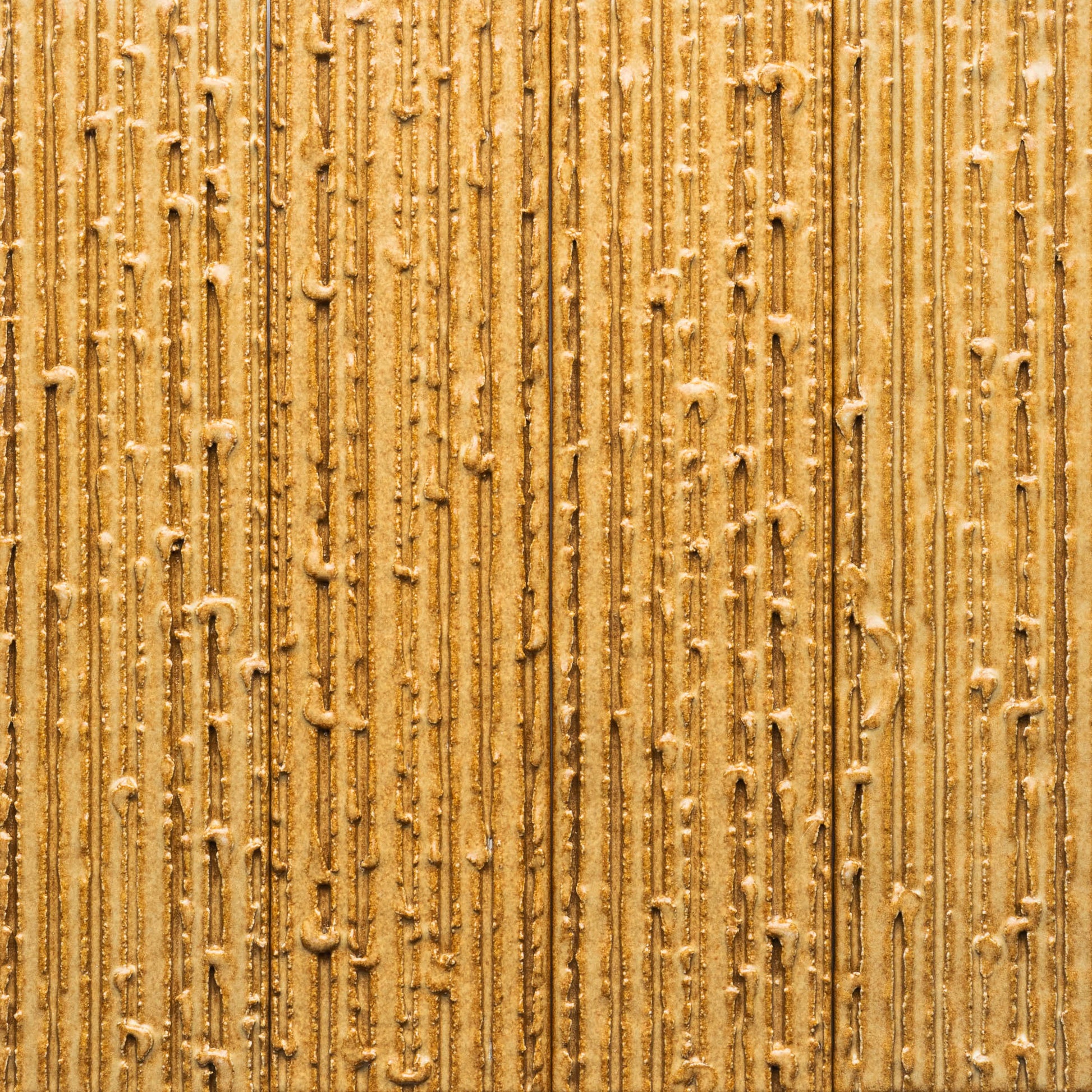 A close-up of Toast + Furrowed by Zia Tile, showing a golden-brown textured surface with vertical, uneven lines and raised bumps, creating a sand-like or heavily frosted appearance.