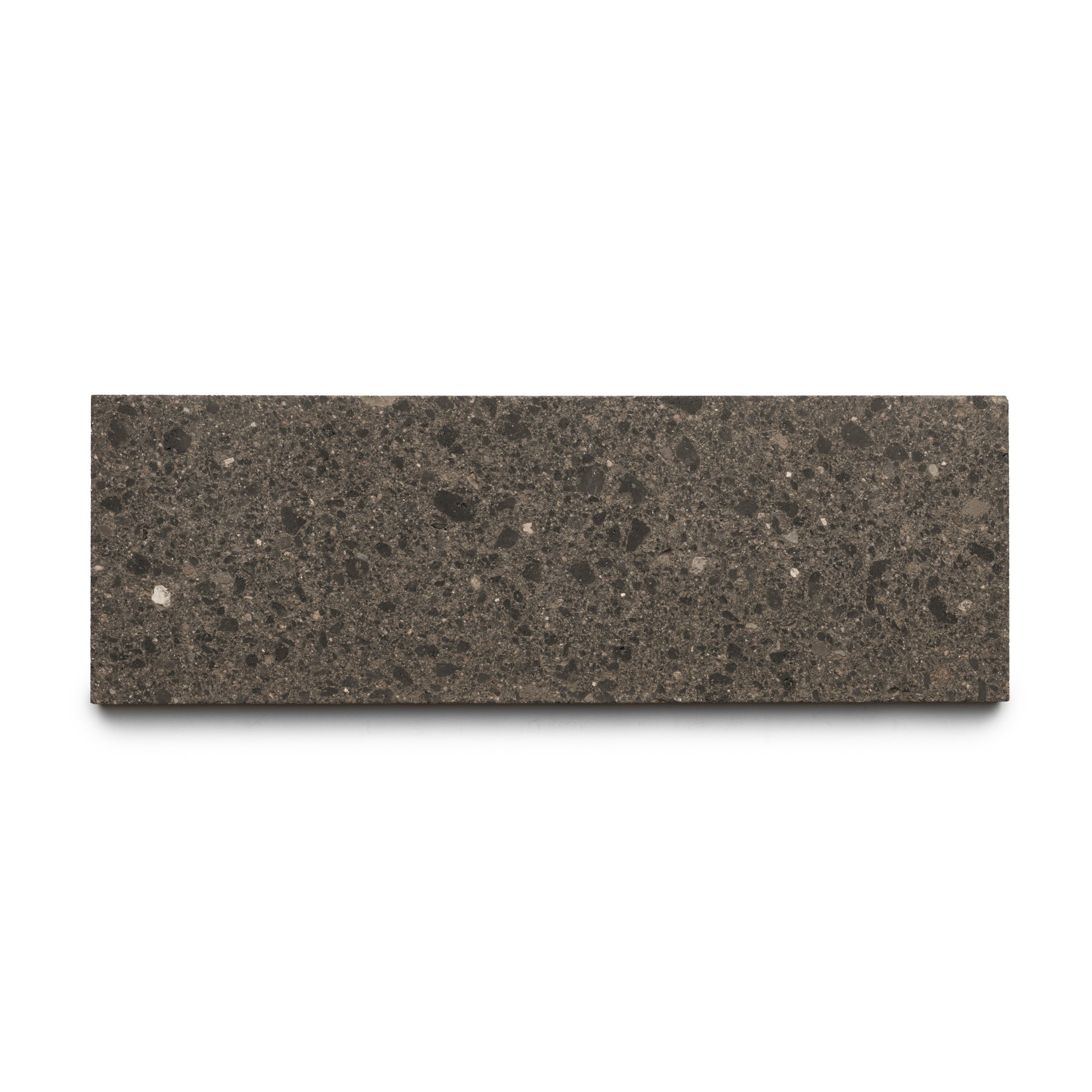 The Volcan 4x12 by Zia Tile is a rectangular dark gray, speckled tile featuring earth-toned aggregates and a smooth, stone-like surface, displayed against a white background.