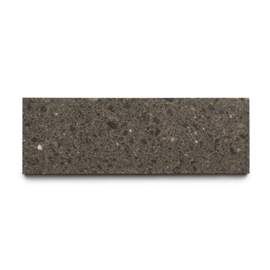 The Volcan 4x12 by Zia Tile is a rectangular dark gray, speckled tile featuring earth-toned aggregates and a smooth, stone-like surface, displayed against a white background.