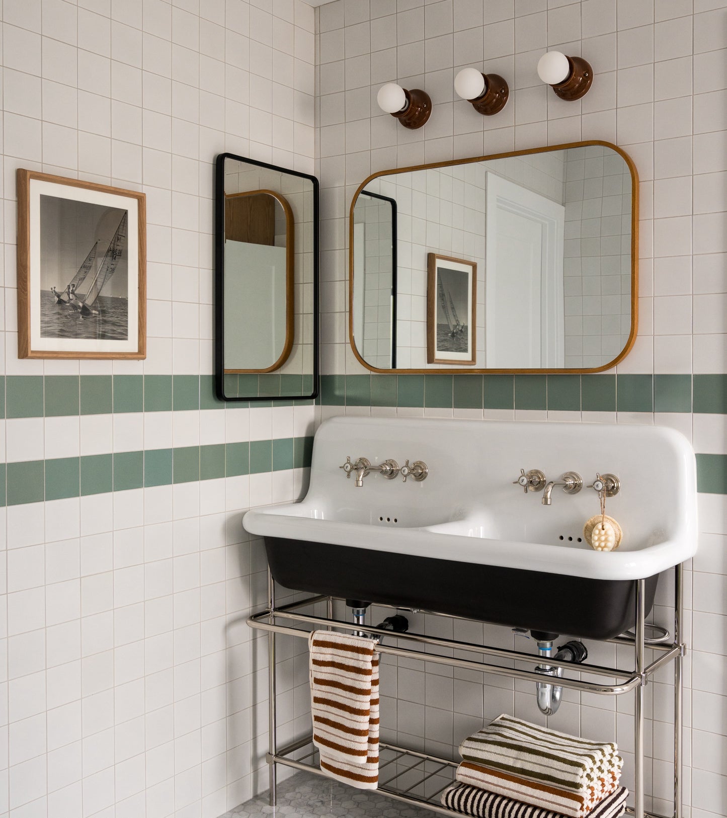 A vintage-style bathroom featuring Zia Tile's Alpha White 4x4 ceramics, a double white sink with chrome fixtures, two mirrors, striped towels, wall-mounted lights, and framed nautical art.